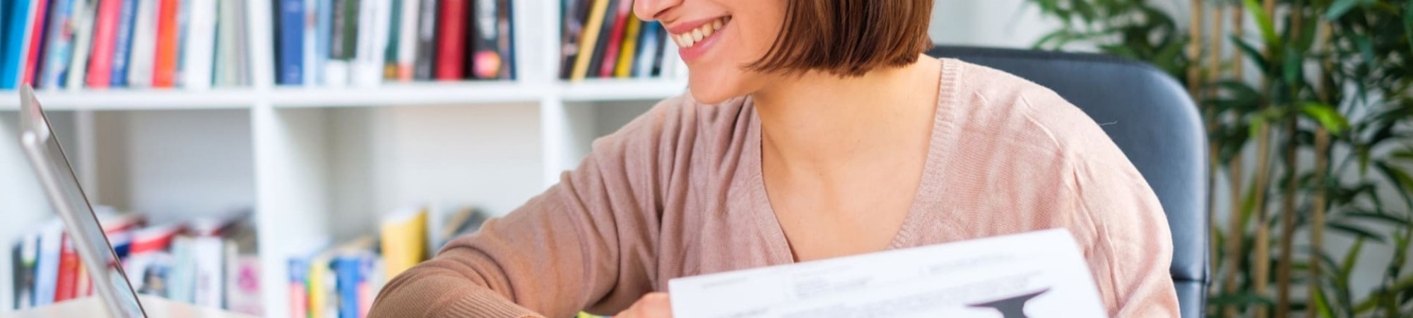 Cheerful woman interviewing job applicant via laptop camera holding a CV